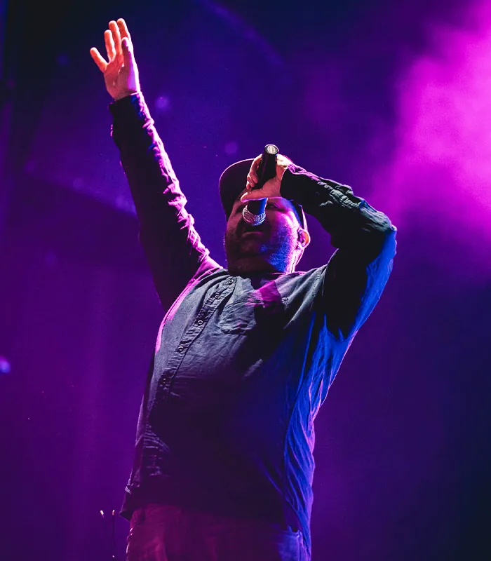 Sänger performt energiegeladen live auf der Bühne im violetten Scheinwerferlicht – Dynamische Bandfotografie, Musikvideos und Event Content in Deutschland.